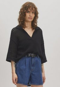 Zwarte gebreide trui met V-hals en kraag, met een losse pasvorm en brede mouwen, gecombineerd met hoge spijkerbroeken in het blauw.