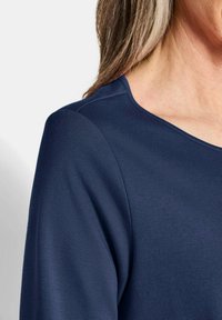 Marineblaue Bluse mit glatter Textur, rundem Ausschnitt und sichtbaren Schulternähten, ausgestattet mit einem taillierten Design, das sich an den Körper anpasst.