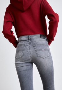 Grijze skinny jeans met een hoge taille, een vijf-pocket ontwerp en een zwart leren merkpatch aan de achterkant. De stof ziet er glad en licht vervaagd uit.