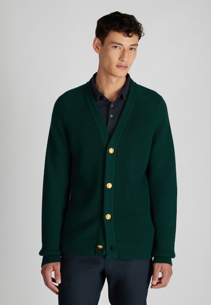 Zielony kardigan z prążkowanej tkaniny, z dekoltem w kształcie litery V i długimi rękawami, ozdobiony złotymi guzikami i teksturowanym wzorem dzianiny.