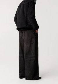 Schwarze cropped Jacke mit strukturiertem Stoff und pelziger Verzierungen, kombiniert mit locker sitzenden dunklen Jeanshosen mit Gesäßtaschen und dezenter Ausbleichung.