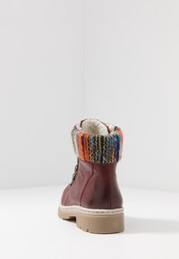 Bota de cuero rojo con un puño de punto multicolor, superficie texturizada, cierre con cordones y suela de goma beige.
