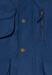 Marineblaue Jacke mit einem Reißverschlussfach und Druckknopfverschluss. Verfügt über mehrere Taschen und eine glatte, weiche Textur. Robuste Stoffoberfläche.