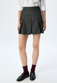 Falda plisada gris hecha de tela texturizada, con una cinturilla ajustada y un diseño acampanado, combinada con mocasines negros y calcetines burdeos.