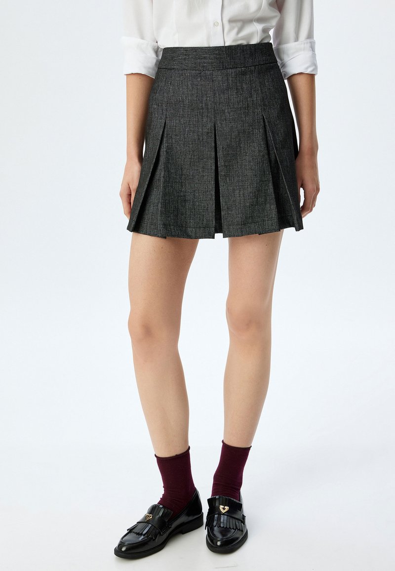 Falda plisada gris hecha de tela texturizada, con una cinturilla ajustada y un diseño acampanado, combinada con mocasines negros y calcetines burdeos.