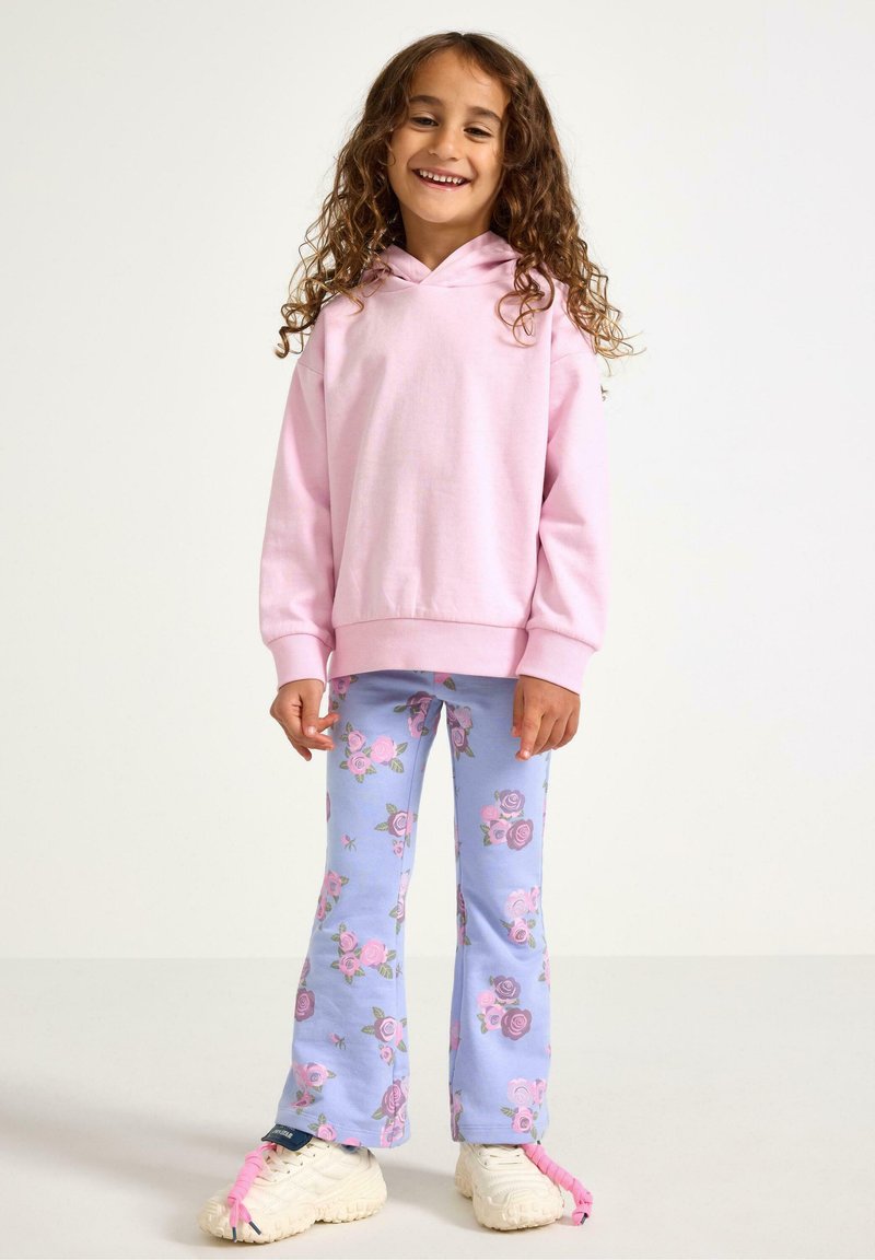 Rosa huvtröja kombinerad med ljusblå utsvängda leggings med rosa blommönster. Vita sneakers med rosa detaljer.