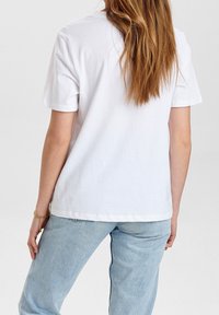 Bílá bavlněná tričko s krátkým rukávem. Má volný střih a jednoduchý design. Kombinováno se světle modrými jeansy.