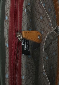 Interno in pelle rossa e beige di una borsa con cerniera e rivestimento in tessuto a fantasia con stelle marroni e dettagli blu. Etichetta del marchio visibile.