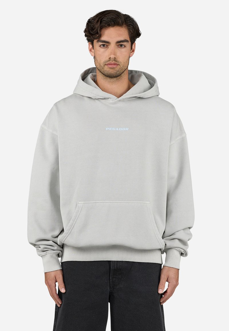 Lys grå oversized hættetrøje med en frontlomme, ribbede manchetter og "PEGADOR" logo i lyseblå på brystet. Blød stoftekstur.