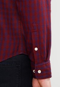 Camicia a maniche lunghe a quadri con strisce rosse e blu navy, dotata di polsini con bottone e orlo leggermente arrotondato. Tessuto testurizzato.
