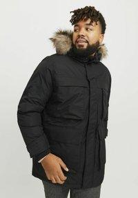 Parka negra con capucha con borde de pelo, que cuenta con grandes bolsillos frontales, cintura ajustada y acentos acolchados en las mangas.