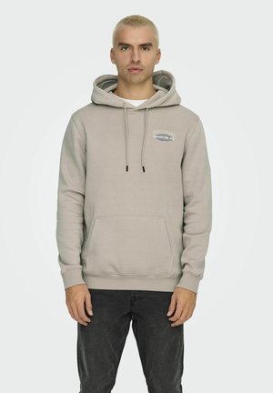 Sudadera beige clara con un bolsillo frontal, cordones y un logo en el pecho. Fabricada con material suave, presenta un ajuste relajado.