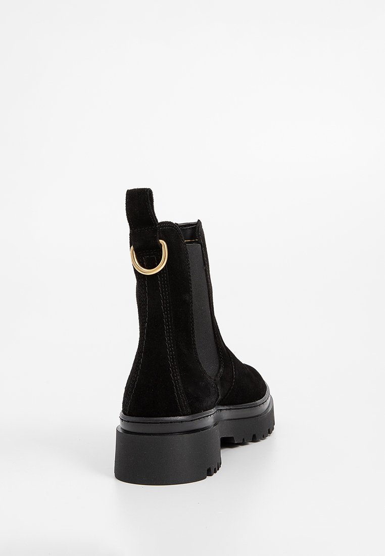 Schwarze Wildleder-Stiefeletten mit strukturierter Oberfläche, elastischen seitlichen Einsätzen und einem goldenen Zugtab. Verfügt über eine klobige schwarze Gummisohle.