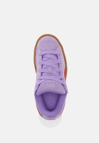 Fialový semišový teniska s kulatou špičkou, tónovanými tkaničkami a červeným akcentem. Má texturovanou podrážku z gumy a vyražené logo na jazyku.