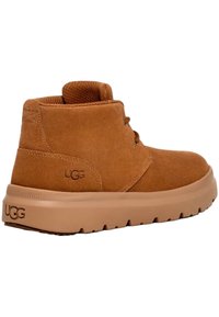 Botas de tobillo de ante color marrón claro con una suela de goma gruesa beige. Presenta dos ojales para cordones y un logo en el costado. Forro de textil suave.