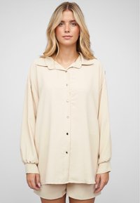 Lys beige skjorte med krage, lange ermer og knapper på mansjettene, laget av mykt stoff, sammen med matchende shorts.