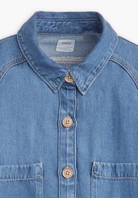 Light blue denim shirt with a classic collar, two chest pockets, brown buttons, and contrasting stitching details.