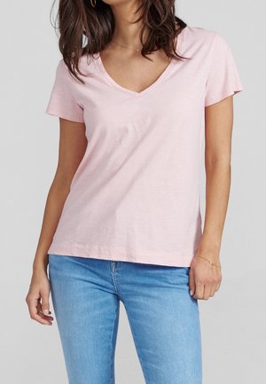 Light pink V-neck t-shirt made from soft cotton fabric, featuring short sleeves and a relaxed fit, paired with blue jeans.