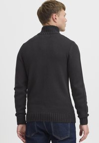 Pull en tricot gris foncé avec un col montant, des poignets et un ourlet côtelés. Présente un motif texturé et une coupe ajustée.