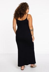 Schwarzes, ärmelloses Maxikleid mit figurnahem Oberteil und fließendem Rock. Weicher Stoff und verstellbare Träger; hat ein einfaches, klassisches Design.