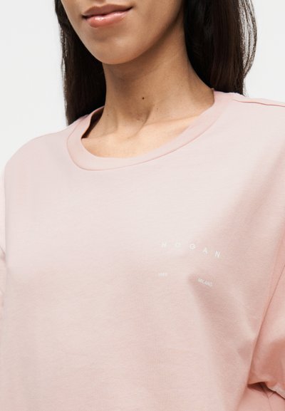Ανοιχτό ροζ βαμβακερό μπλουζάκι με στρογγυλή λαιμόκοψη. Διαθέτει λευκή εκτύπωση με το λογότυπο "HOGAN", "1986" και "MILANO" στο στήθος.