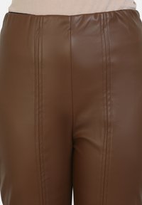 Bruine nepleder broek met een gladde textuur, voorzien van verticale naden aan beide voorkanten en een elastische tailleband.