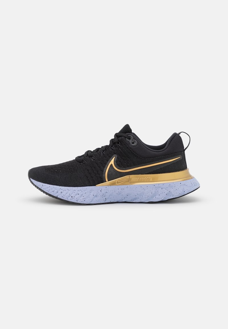 Chaussure de running Nike noire et dorée avec tige en maille texturée, semelle blanche tachetée et logo Swoosh doré sur le côté.