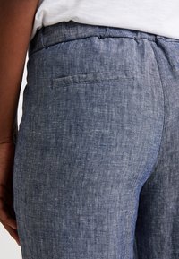 Světle modré lněné kalhoty s texturovaným povrchem, vybavené zadní kapsou a elastickým pasem pro pohodlí. Detaily jsou decentní a přizpůsobené.