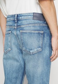 Lichtblauwe spijkerbroek met een rechte snit, voorzien van twee achterzakken en een leren label met de naam "Marc O'Polo DENIM."