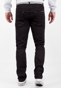 Zwarte denim jeans met een slim fit, voorzien van achterzakken met patroonstiksel. Vergezeld van witte Converse sneakers.
