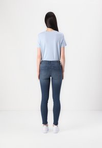 Vaaleansininen lyhythihainen t-paita yhdistettynä tummansinisiin skinny-farkkuihin ja valkoisiin kenkiin, nähtynä takaa. Minimalistinen muotoilu, sileä tekstuuri.