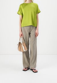 Haut en satin vert à manches courtes associé à un pantalon large à rayures beige et blanc. Tongs noires et sac à main multicolore avec poignée tressée.