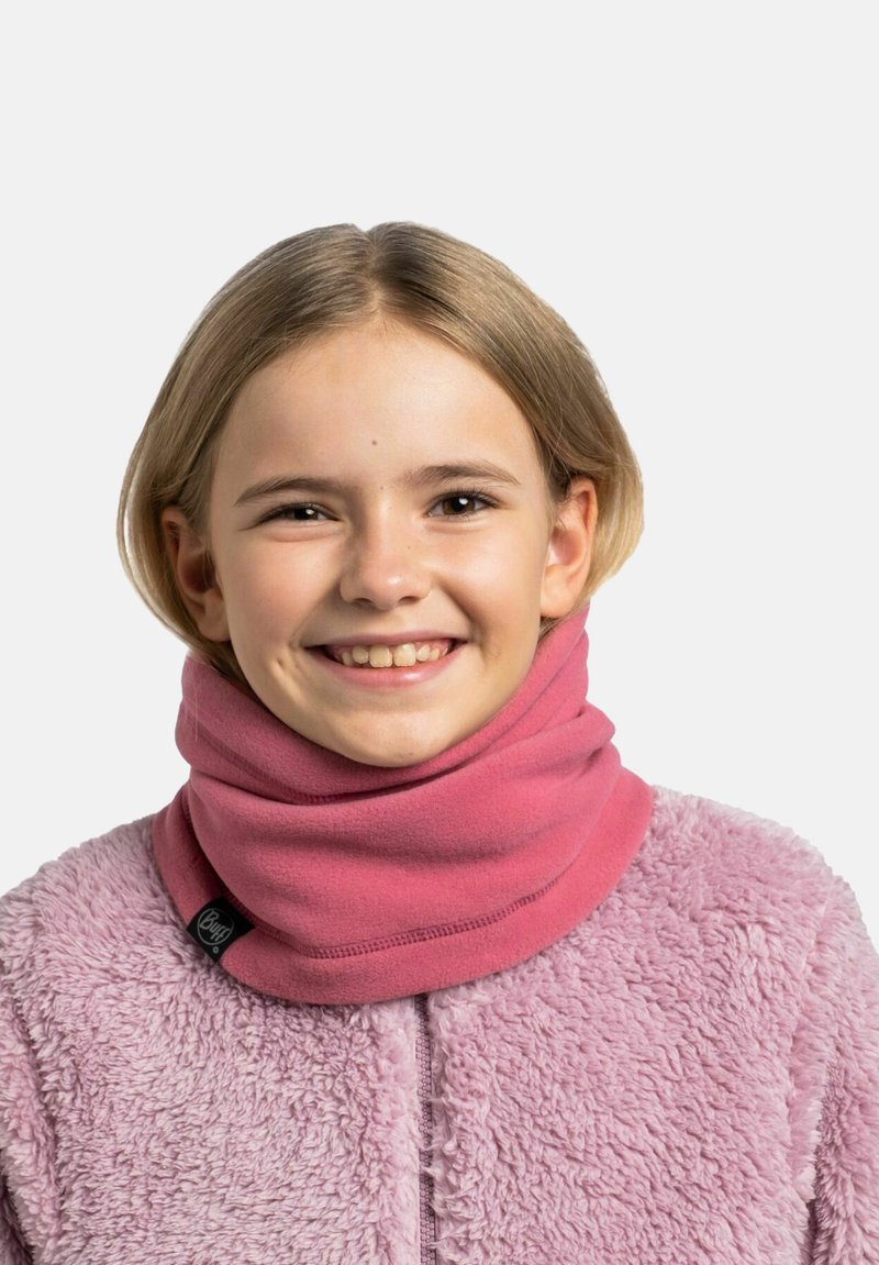 Niño sonriente con cabello rubio corto, que lleva una chaqueta de forro polar rosa y un cubrecuello rosa, frente a un fondo liso.