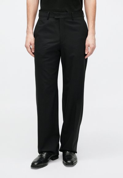 Μαύρο παντελόνι με ευθεία γραμμή, με επίπεδη πρόσοψη, θηλιές για ζώνη και ομαλή υφή. Φορεμένο με μαύρα παπούτσια.