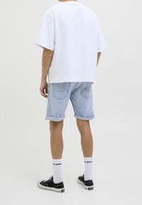 T-shirt bianca in cotone, vestibilità ampia, abbinata a pantaloni corti in denim azzurro. Sneakers nere con suole bianche e calzini a fantasia. Sfondo neutro.