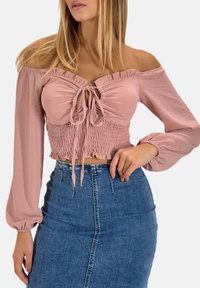 Blusa leggera rosa pallido con spalle scoperte, vita arricciata, scollatura a volant e chiusura con fiocco, abbinata a una gonna in denim a vita alta.