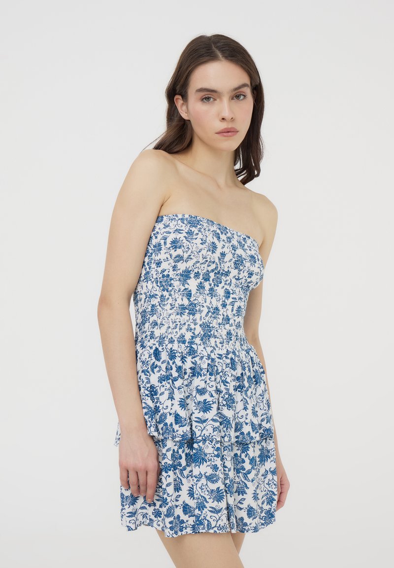 Abito senza spalline con un motivo floreale blu e bianco. Presenta strati arricciati e un corpetto elasticizzato per una silhouette aderente.
