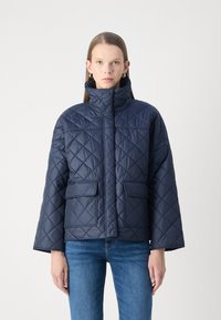 Ναυτικό καπιτονέ μπουφάν με ψηλό γιακά, δύο μπροστινές τσέπες και άνετη εφαρμογή. Κατασκευασμένο από λεία, γυαλιστερή ύλη με διαμαντένιο μοτίβο.