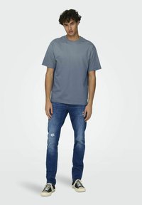 Grijze gradient t-shirt met korte mouwen, gecombineerd met vervaagde blauwe jeans met distressed accenten en zwarte sneakers.