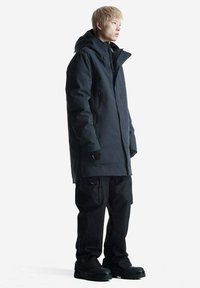 Parka impermeabile nera con cappuccio regolabile, tasche con cerniera e vestibilità comoda, abbinata a pantaloni cargo neri e stivali neri resistenti.