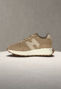 Baskets en daim beige avec logo latéral crème, semelle intermédiaire blanche, semelle extérieure en gomme naturelle et lacets beiges, présentées sur une surface et un fond neutres.