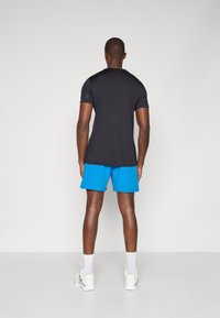 Camisa preta de manga curta, calções desportivos azuis e ténis brancos. Tecido suave, design ajustado e textura leve.