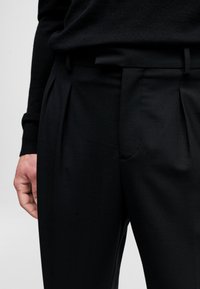 Černé skládací kalhoty z hladkého materiálu s klasickým střihem, postranními kapsami a čistým pasem pro upravený vzhled.