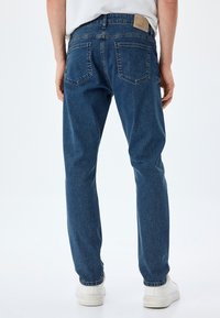 Jeans de denim azul con un corte relajado, diseño de cinco bolsillos y una etiqueta de cuero en la cintura trasera. Tejido texturizado con un acabado desgastado.