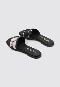 Chanclas negras con un acento de cadena dorada, con un upper plateado texturizado y una suela negra lisa. Logo impreso en la plantilla.