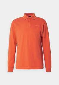 Pitkähihainen oranssi polo-paita, jossa on kaksi nappia, ribbireunukset ja huomaamaton brodeerattu logo vasemmassa rinnassa.