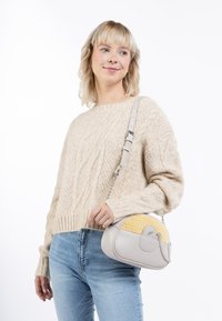 Crossbody taske med en lys grå læderkrop, gul tekstureret accent, rund form, kædesnor og et mærke-detalje på forsiden.
