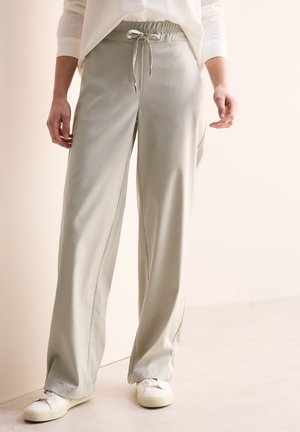 Pantaloni a gamba larga grigio chiaro realizzati in tessuto morbido, con cintura elastica e cordino, abbinati a sneaker bianche.