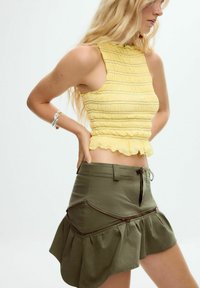 Top corto giallo arricciato con orlo a balze abbinato a una gonna verde kaki con zip diagonali e orlo a campana asimmetrico.