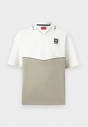 Polo a maniche corte con metà superiore bianca, metà inferiore beige, rifiniture nere e piccolo logo floreale nero con scritta "HUGO" sul petto.